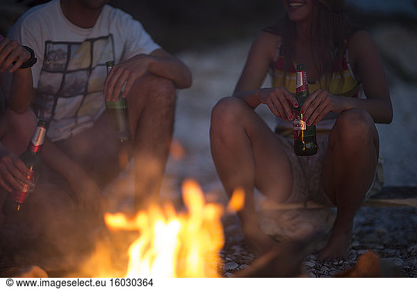 A group of young people gathered on a beach around a campfire.