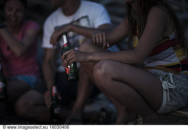 A group of young people gathered on a beach drinking beer.