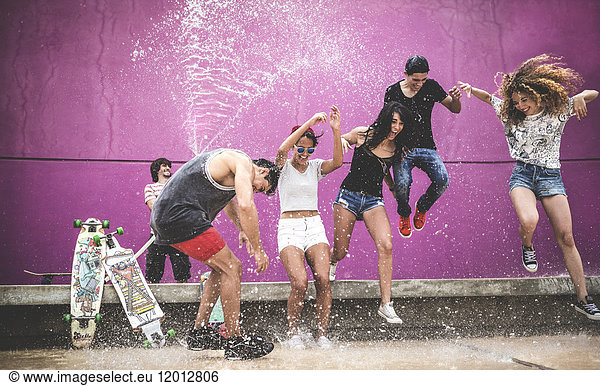 A group of young people jumping while being sprayed with water.