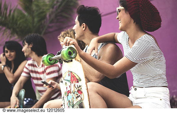 A group of young people sitting down  one holding a skateboard.