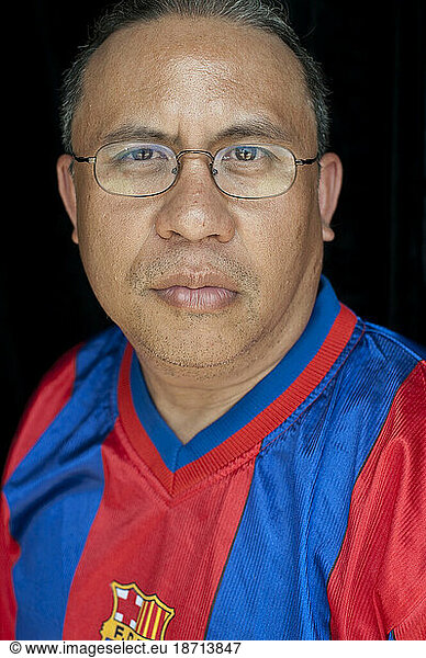 A Guatemalan man wearing glasses and a soccer jersey stands for a portrait.