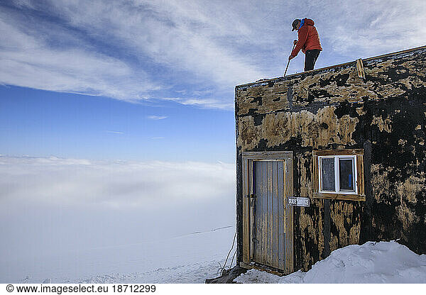 A Guide Cleans the Roof of a Shelter at Camp Muir  Mount Rainier
