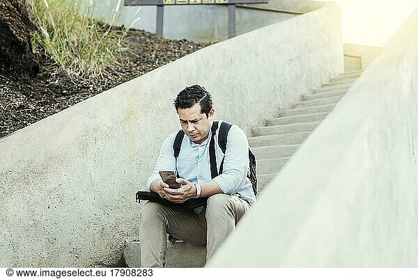 A guy sitting on stairs using his cell phone outdoors with copy space  Young man sitting on stairs using smart phone  Close up of young man sitting on stairs texting on cell phone outdoors
