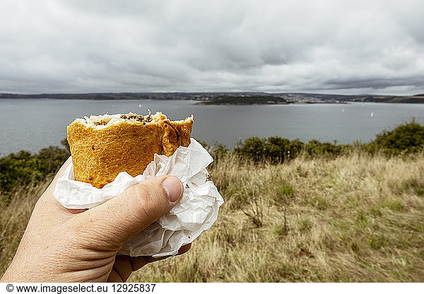 A hand holding a half eaten Cornish pasty.