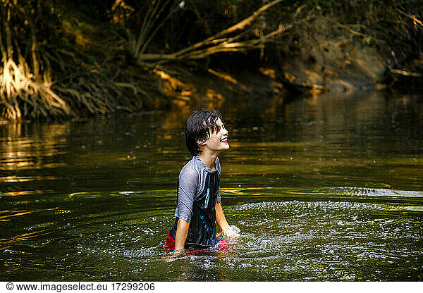 A happy boy plays in a river in golden sunlight in summertime