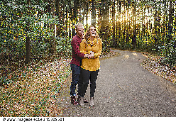 A happy couple hold each other close on a forest pathway at sunset