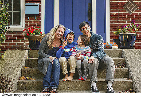 A happy family sit together on the front stoop of their home smiling