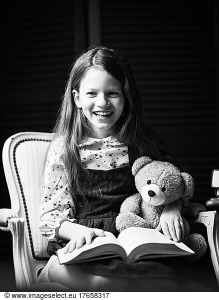A happy girl reads a fun story with a teddy bear.
