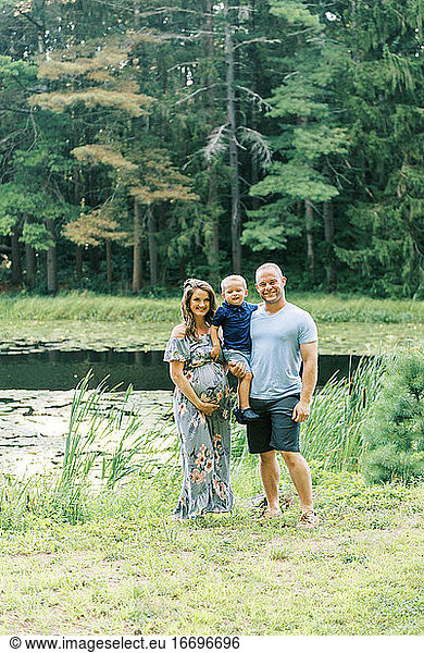 A happy growing family standing by a pond