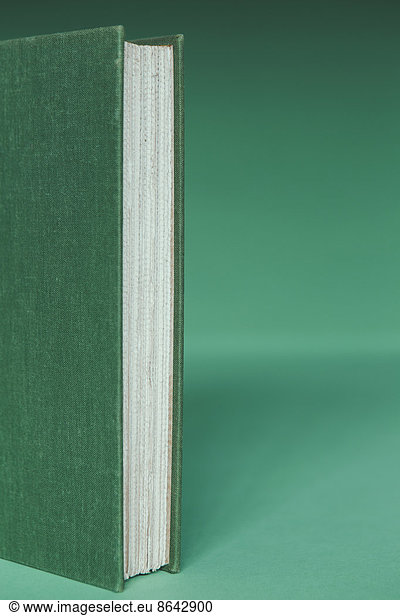 A hard cover book with a green cover  and white paper page edges  upright on a green background.