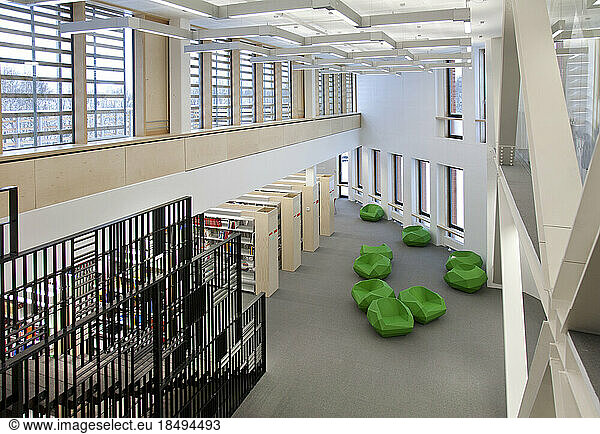 A healthcare college library with open spaces  green chairs and book stacks. A modern light and airy building.