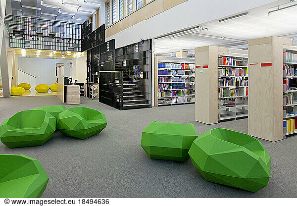 A healthcare college library with open spaces  green chairs and book stacks. A modern light and airy building.
