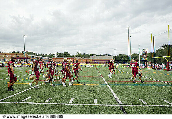 A high school football team walk across field against cloudy sky