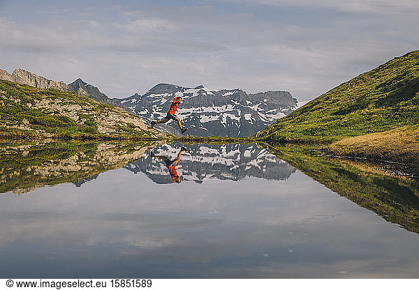 A hiker is jumping reflected in a mountain lake in Chamonix Valley.