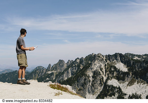 A hiker on the mountain summit  looking at a map. Surprise Mountain  Alpine Lakes Wilderness  in Mount Baker-Snoqualmie National Forest