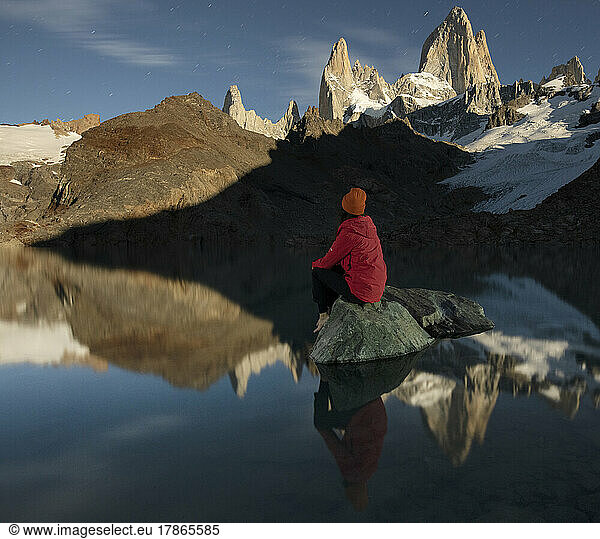A hiker sits on a rock in Laguna de los Tres in front of the ico
