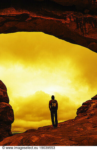 A hiker stands under a natural arch in Arches National Park.