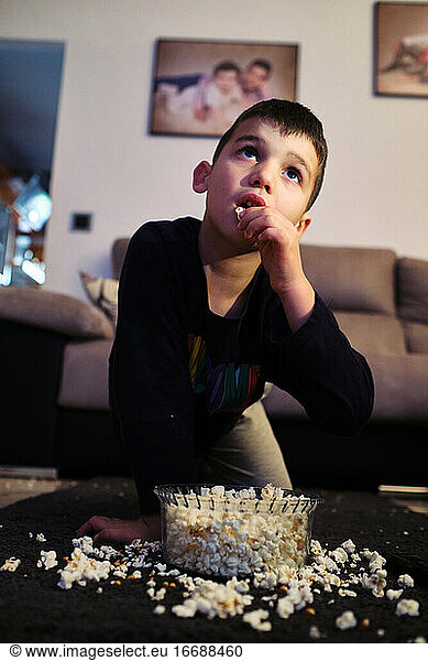 a kid eats popcorn at home while watching a movie