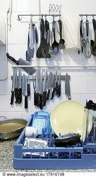 A kitchen with dishes in a rack and hanging storage of knives and kitchen utensils