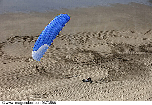 A kite buggy rolls through shapes and textures in the sand on a beach.
