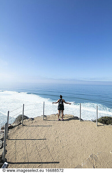 A lady with backpack looks at the ocean during a hike in San Diego