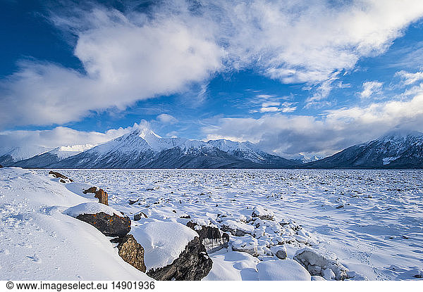 A landscape of clouds over the frozen Cook Inlet in South-central Alaska with the Chugach Mountains in the background on a winter day; Alaska  United States of America