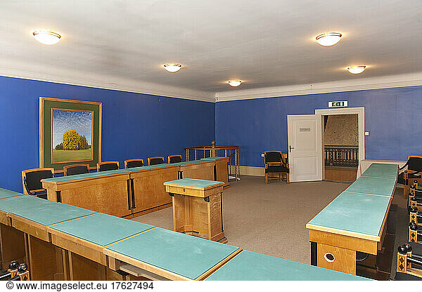A large meeting room  with desks and chair and central podium  old fashioned decor  bright blue walls