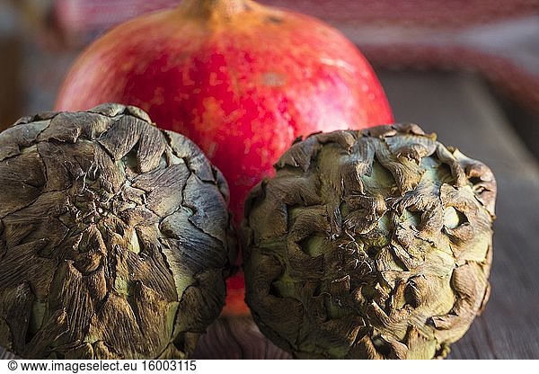 A large pomegranate and two artichokes siting on a wooden surface.