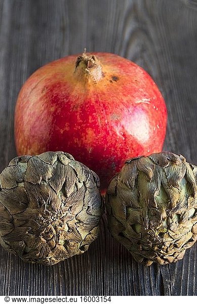 A large pomegranate and two artichokes siting on a wooden surface.