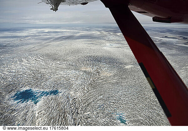 A large pool of water remains on the surface of the ice cap as the Twin Otter aeroplane flies over the ice. Surface structure of the glacier is apparent. Photograph taken through the window of the Twin Otter aeroplane enroute to Centrum S?? from Mestersvig.; Northeast Greenland   Greenland