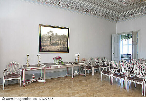 A large room with parquet flooring  elegant chairs and tables.
