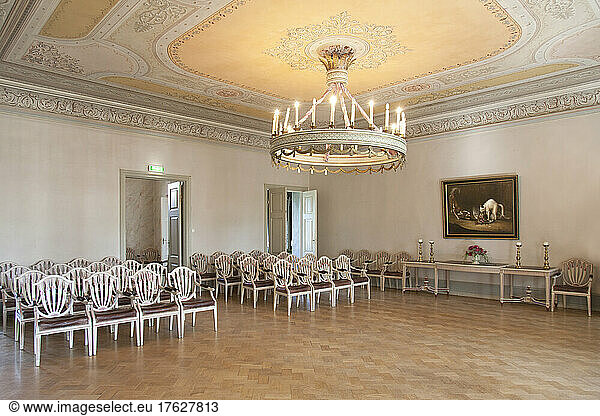 A large room with parquet flooring  elegant chairs and tables  chandelier and dance floor.