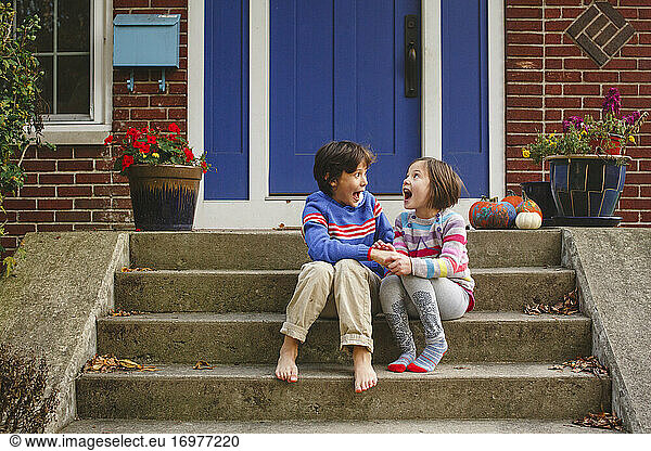 A little boy and girl sitting on stoop yell out loud in joy together