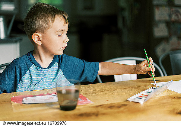 A little boy painting with watercolors at a table