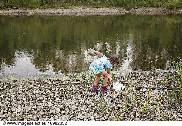 A little girl cleans litter up off of the shoreline of a river