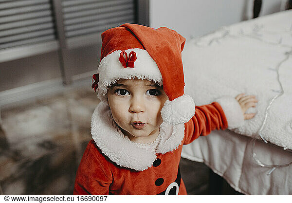 A little girl disguised as Santa Claus looking at the camera.