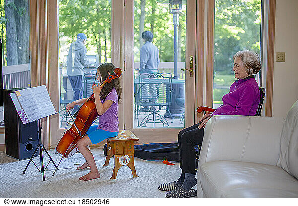 A little girl gives cello concert to grandmother inside