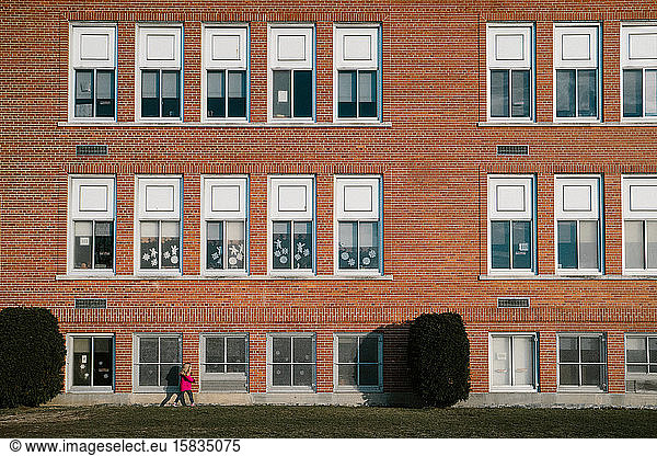 A little girl in a pink coat walks past a school building.