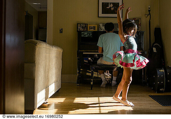 A little girl in tutu raises her arm to dance to father's piano music