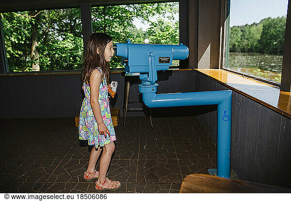 A little girl looks out through large binoculars at birds on pond