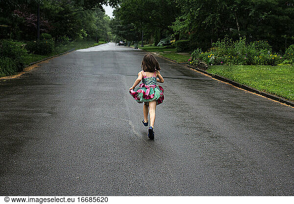 A little girl runs down an empty street in a brightly colored tutu