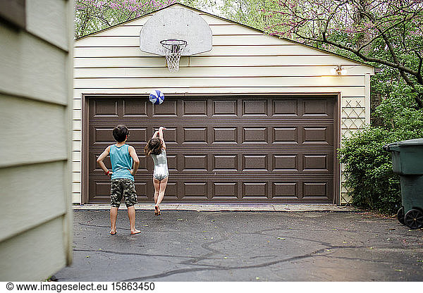 A little girl shoots a basketball while her big brother watches on