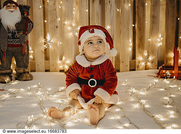 A little girl sitting in a Santa Claus outfit.