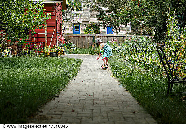 A little girl skateboards down a path through backyard garden