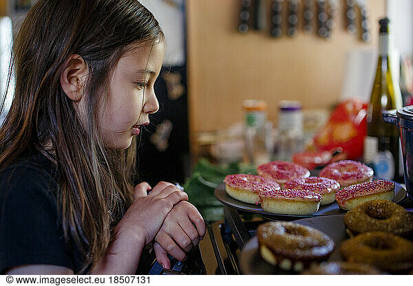 A little girl stares longingly at donuts on countertop