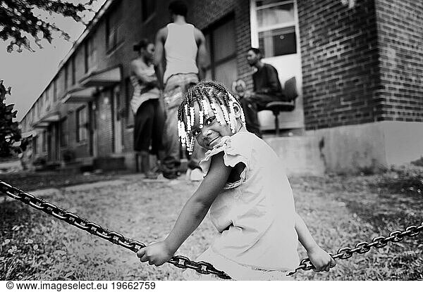 A little girl swings on the chain in the parking lot of government housing.