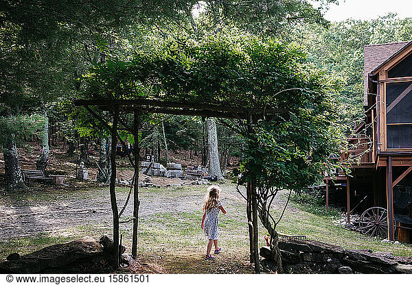 A little girl walks under an arbor.