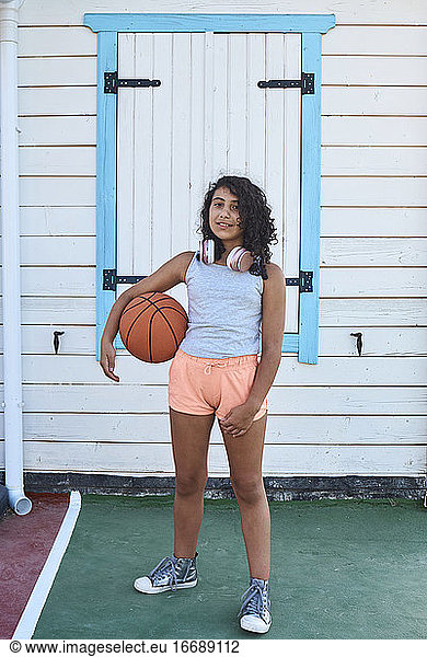 A little girl with curly hair and a basketball looking at the camera