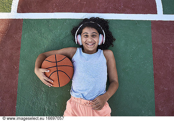 A little girl with curly hair is lying on a basketball court laughing