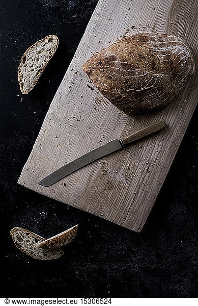 A loaf of brown bread on a board and a bread knife